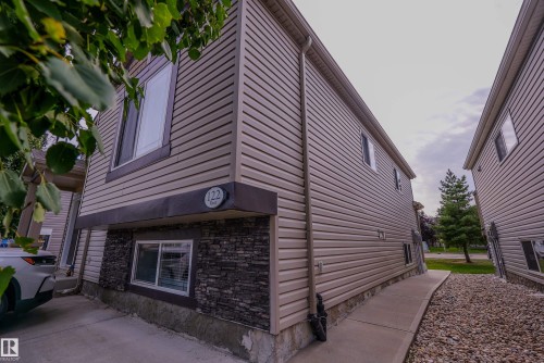 Modern townhome exterior featuring horizontal siding, stone veneer accents at the foundation, large multi-pane windows, and a paved entryway with mature landscaping - 122 142 Selkirk Place, Leduc, AB 