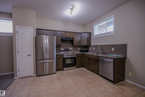 Kitchen featuring stainless steel appliances, dark wood-finish cabinetry, tile flooring, and a stone-finish countertop - 122 142 Selkirk Place, Leduc, AB 