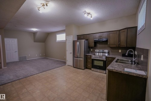 Kitchen featuring dark wood-finish cabinetry, stainless steel appliances, and a double basin sink - 122 142 Selkirk Place, Leduc, AB 