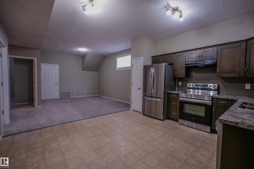 Kitchen with dark wood-finish cabinetry, stainless steel appliances, and a double basin sink - 122 142 Selkirk Place, Leduc, AB 