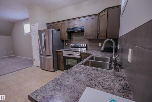 Kitchen featuring dark wood-finish cabinetry, stainless steel appliances, a double basin sink, and a mottled countertop - 122 142 Selkirk Place, Leduc, AB 