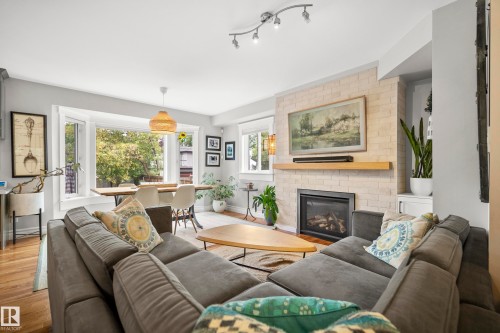 Living area with wood-finish flooring, a contemporary fireplace featuring a light brick surround and wood mantle, and track lighting - 11006 64 Avenue Nw, Edmonton, AB 