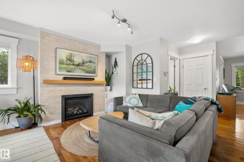 Fireplace with a natural wood mantel, light-toned brick surround, and black firebox - 11006 64 Avenue Nw, Edmonton, AB 