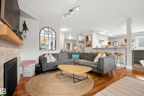 Warm wood-finish flooring, fireplace with a light brick surround, built-in wooden mantel, kitchen with a breakfast bar, and recessed lighting - 11006 64 Avenue Nw, Edmonton, AB 