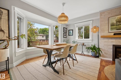 Bay window with ample natural light, light wood-finish flooring, recessed fireplace with light brick surround, wood mantel, and a woven pendant light fixture - 11006 64 Avenue Nw, Edmonton, AB 