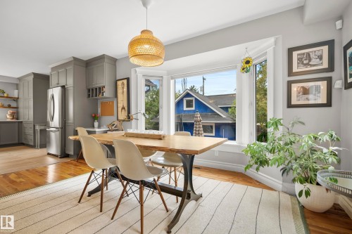 Open-concept kitchen and dining area featuring a bay window, wood-finish flooring, and gray cabinetry with stainless steel appliances - 11006 64 Avenue Nw, Edmonton, AB 