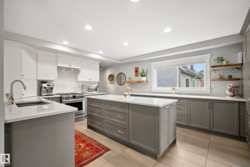 Modern kitchen featuring a central island with integrated storage, light-toned countertops, contrasting grey and white cabinetry, recessed lighting, and a stainless steel range with matching hood - 11006 64 Avenue Nw, Edmonton, AB 