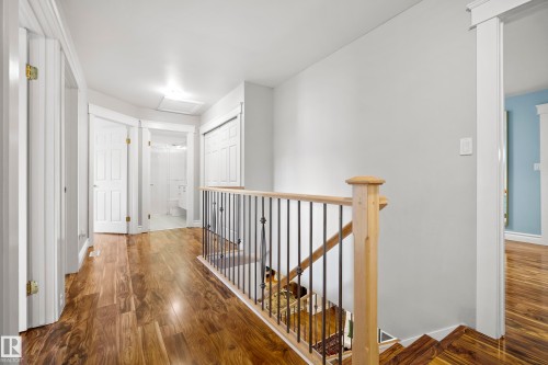 Hallway featuring wood-finish flooring, white trim, light gray walls, and a staircase with an iron spindle railing and wood handrail - 11006 64 Avenue Nw, Edmonton, AB 