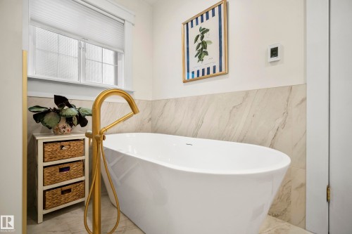 Freestanding soaking tub with a floor-mounted brass-finish faucet, complemented by a tiled accent wall - 11006 64 Avenue Nw, Edmonton, AB 