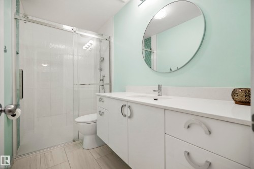 Bathroom featuring a glass-enclosed shower, white tile walls, a floating vanity with a white countertop, and wood-finish flooring - 11006 64 Avenue Nw, Edmonton, AB 