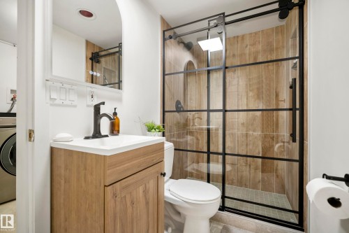 Bathroom featuring a vanity with a white countertop, a black-framed sliding glass shower enclosure, wood-finish wall tile, and a tile shower pan - 11006 64 Avenue Nw, Edmonton, AB 