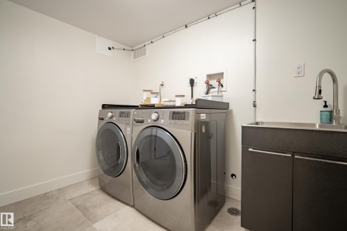 Utility room with gray tile flooring, stainless steel sink, dark cabinetry, and wall-mounted faucet - 11006 64 Avenue Nw, Edmonton, AB 