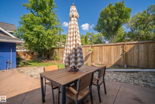 Expansive concrete patio with a paver stone inlay, featuring a wood privacy fence and a verdant lawn area - 11006 64 Avenue Nw, Edmonton, AB 