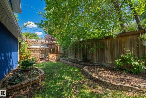 Fenced backyard featuring a wood pergola, stone-lined garden beds, and mature trees - 11006 64 Avenue Nw, Edmonton, AB 