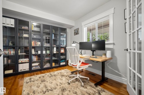 Built-in cabinetry with glass panel doors, wood-finish flooring, a window with white trim, and a French door - 11006 64 Avenue Nw, Edmonton, AB 