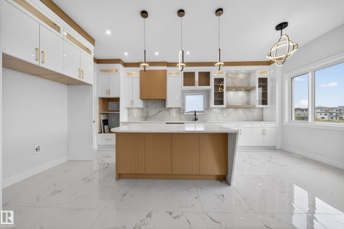 Quartz countertops, white high-gloss cabinetry, wood-finish island, geometric pendant lighting, and large windows - 8737 Mayday Lane Sw, Edmonton, AB 