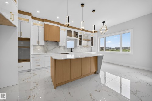 Modern kitchen featuring white and wood-finish cabinetry, a large kitchen island with a white countertop, and a matching full-height backsplash - 8737 Mayday Lane Sw, Edmonton, AB 