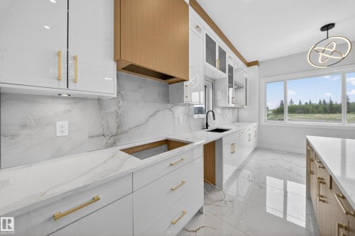 Sleek kitchen with white cabinetry and gold-tone hardware, featuring integrated wood-finish elements - 8737 Mayday Lane Sw, Edmonton, AB 