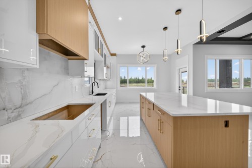 Gleaming white large format floor tiles, extensive white stone-finish countertops and backsplash, light wood-finish cabinetry, contemporary pendant lighting, and multiple windows - 8737 Mayday Lane Sw, Edmonton, AB 