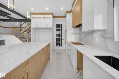 Spacious kitchen featuring an expansive island, white cabinetry, light wood-finish accents, large format floor tiles, and a coordinated backsplash - 8737 Mayday Lane Sw, Edmonton, AB 