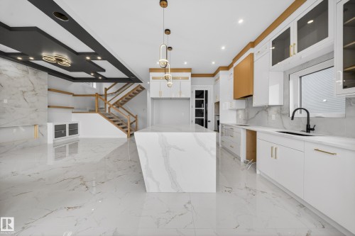 Sophisticated kitchen featuring a waterfall-edge island with polished stone countertops, white cabinetry with brass hardware accents, stainless steel appliances, and a matte black faucet - 8737 Mayday Lane Sw, Edmonton, AB 