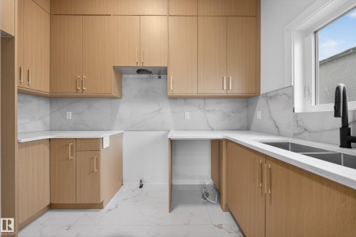 Kitchen featuring light wood-finish cabinetry, white countertops, marble-look backsplash, stainless steel double basin sink, and a matte black gooseneck faucet - 8737 Mayday Lane Sw, Edmonton, AB 