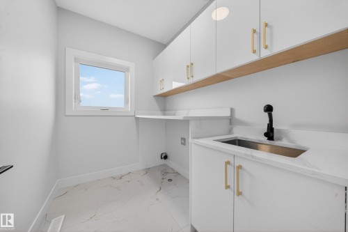 White cabinetry with gold-tone hardware, undermount sink with a black faucet, light-toned countertop, and patterned floor tile - 8737 Mayday Lane Sw, Edmonton, AB 