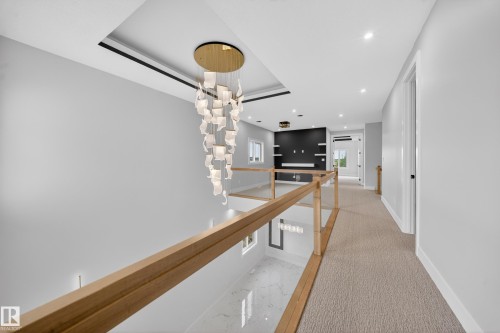 Contemporary chandelier with a gold-tone base, recessed ceiling lighting, light-toned carpeting, and light wood-tone railings with glass panels - 8737 Mayday Lane Sw, Edmonton, AB 