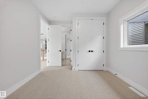 Neutral carpet flooring, white walls, white trim, white doors with matte black hardware, and a window with white trim - 8737 Mayday Lane Sw, Edmonton, AB 