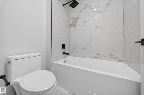 Bathtub with a shower featuring large format veined wall tiles, a matte black rain shower head, and coordinating matte black fixtures - 8737 Mayday Lane Sw, Edmonton, AB 