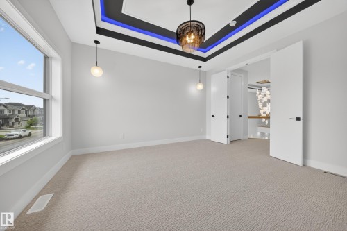Recessed ceiling design with accent lighting, contemporary chandelier, double doors, large window, and light-toned carpet flooring - 8737 Mayday Lane Sw, Edmonton, AB 