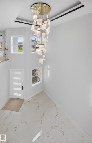 Two-story foyer featuring a sculptural chandelier, light-toned tile flooring, contemporary entryway door, and multiple windows providing ambient light - 8737 Mayday Lane Sw, Edmonton, AB 