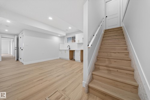 Light wood-finish flooring, recessed lighting, white cabinetry, subway tile backsplash, and a modern matte black faucet - 8737 Mayday Lane Sw, Edmonton, AB 