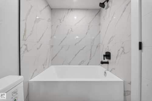 Built-in tub with matte black fixtures, white marble-style tile surround, and recessed ceiling lighting - 8737 Mayday Lane Sw, Edmonton, AB 