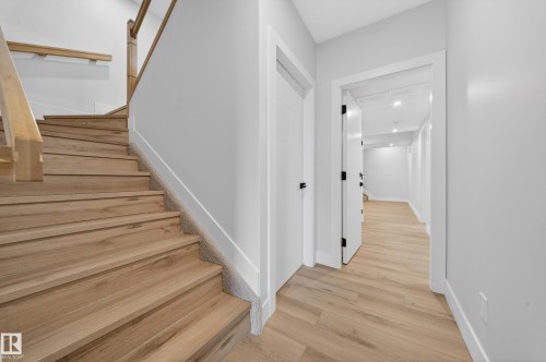 Wood-finish staircase with natural wood handrail, light wood-finish flooring, white walls, and recessed lighting - 8737 Mayday Lane Sw, Edmonton, AB 