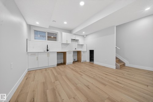 Bright open space featuring wood-finish flooring, recessed lighting, and a white cabinet system with a subway tile backsplash - 8737 Mayday Lane Sw, Edmonton, AB 
