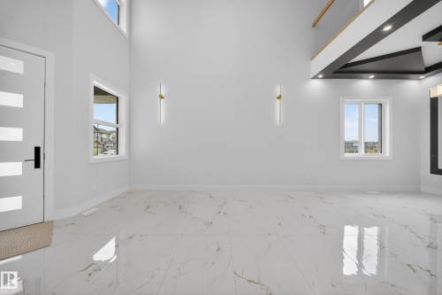 Double-height ceiling, large format tile flooring, contemporary wall sconces, multiple windows, and a modern interior door with frosted glass panels - 8737 Mayday Lane Sw, Edmonton, AB 