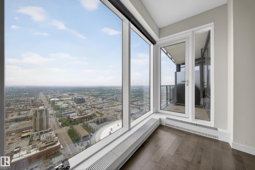 Expansive floor-to-ceiling windows, wide plank wood-finish flooring, white trim, and a glass-paneled exterior door leading to a balcony - #4007 10360 102 St Nw, Edmonton, AB 
