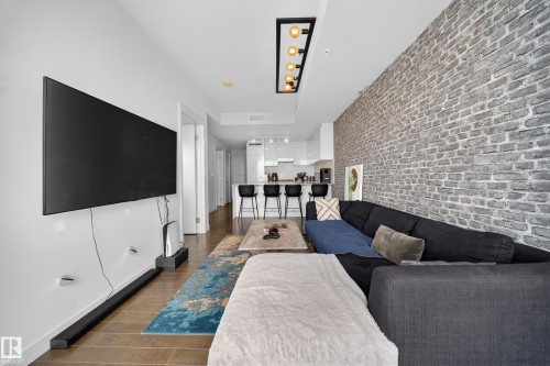 Living area featuring a textured brick accent wall, wood-finish flooring, and a modern linear chandelier - #4007 10360 102 St Nw, Edmonton, AB 