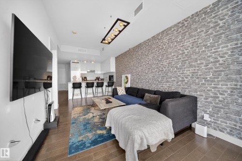 Open-concept living space featuring wood-finish flooring, an exposed brick accent wall, and a linear overhead light fixture - #4007 10360 102 St Nw, Edmonton, AB 