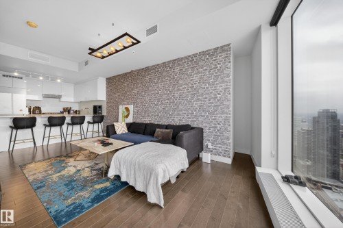 Hardwood-finish flooring throughout, exposed brick accent wall, floor-to-ceiling windows, recessed lighting, and a linear pendant light fixture - #4007 10360 102 St Nw, Edmonton, AB 