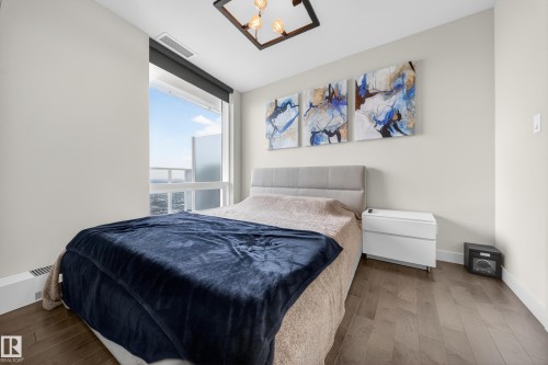 Hardwood-style flooring, white walls, large window with roller shade, modern ceiling fixture, and a light gray upholstered headboard - #4007 10360 102 St Nw, Edmonton, AB 