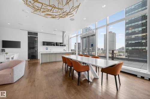 Expansive windows with city backdrop, wood-finish flooring, modern kitchen island, built-in range hood, and contemporary ceiling light fixture - #4007 10360 102 St Nw, Edmonton, AB 