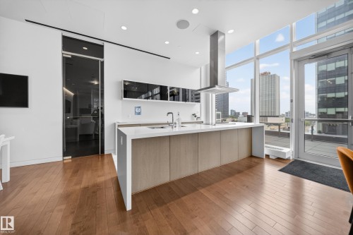Open-concept kitchen featuring wood-finish flooring, a central island with an integrated sink and light wood-tone cabinetry, a stainless steel range hood, and floor-to-ceiling windows - #4007 10360 102 St Nw, Edmonton, AB 