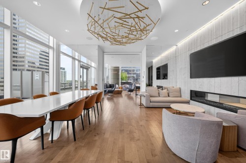 Open-concept living space with expansive windows, wood-finish flooring, a contemporary linear fireplace, and a striking overhead light fixture - #4007 10360 102 St Nw, Edmonton, AB 