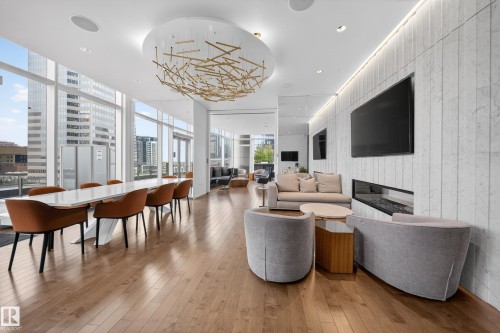 Wood-finish flooring throughout, full-height window wall, contemporary linear chandelier, integrated linear fireplace, and ceiling-mounted light fixtures - #4007 10360 102 St Nw, Edmonton, AB 