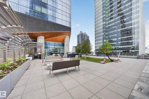 Expansive paved terrace with integrated planters, a pergola structure, and a dedicated grassy area with mature trees - #4007 10360 102 St Nw, Edmonton, AB 