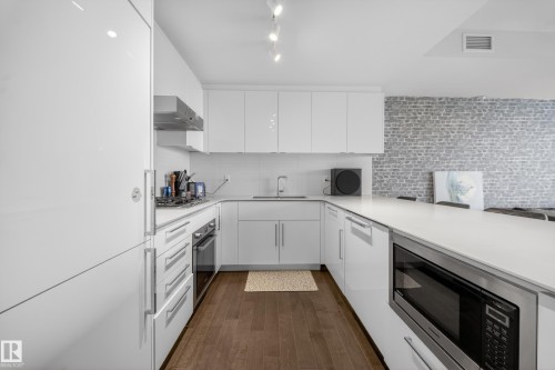 Modern kitchen featuring white cabinetry, integrated stainless steel appliances, a built-in microwave, and wood-finish flooring - #4007 10360 102 St Nw, Edmonton, AB 
