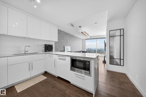 Modern kitchen featuring white cabinetry, integrated stainless steel microwave, and wood-finish flooring - #4007 10360 102 St Nw, Edmonton, AB 