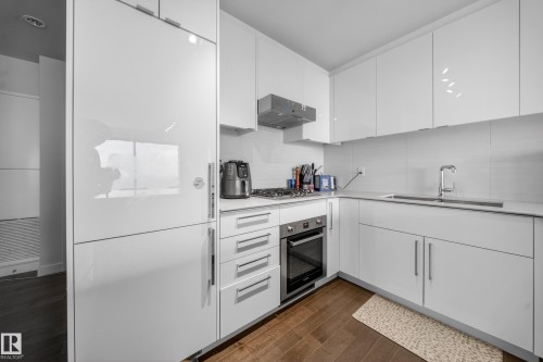 Sleek kitchen featuring white flat-panel cabinetry, a built-in refrigerator, stainless steel appliances, and wood-finish flooring - #4007 10360 102 St Nw, Edmonton, AB 